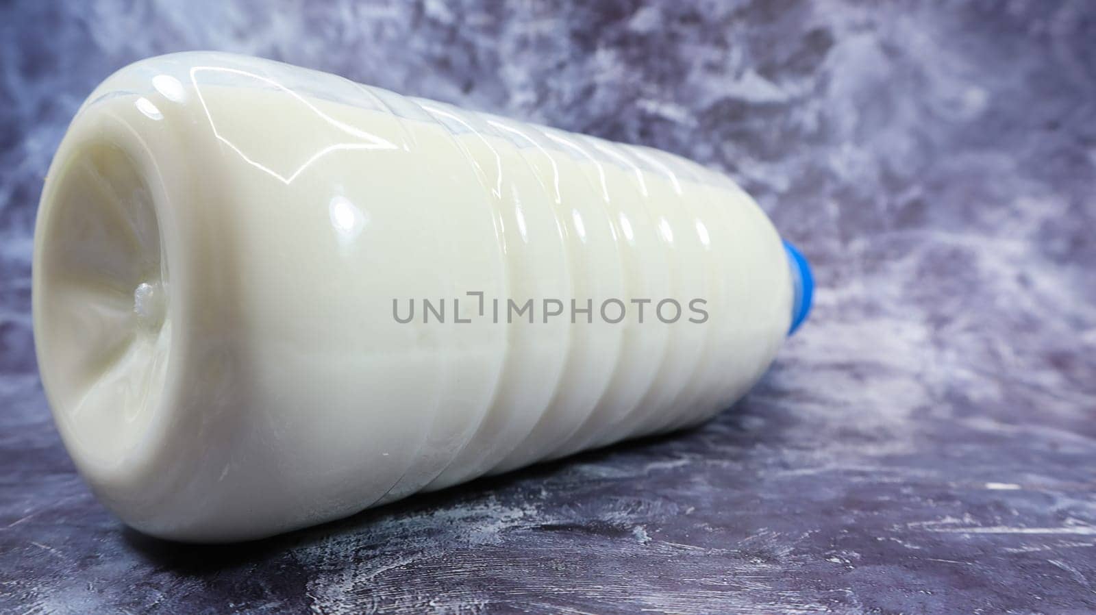 A plastic bottle with a blue cap of fresh regular milk on a dark gray marbled or concrete background. Close-up front view. World milk day concept. Nutrient fluid