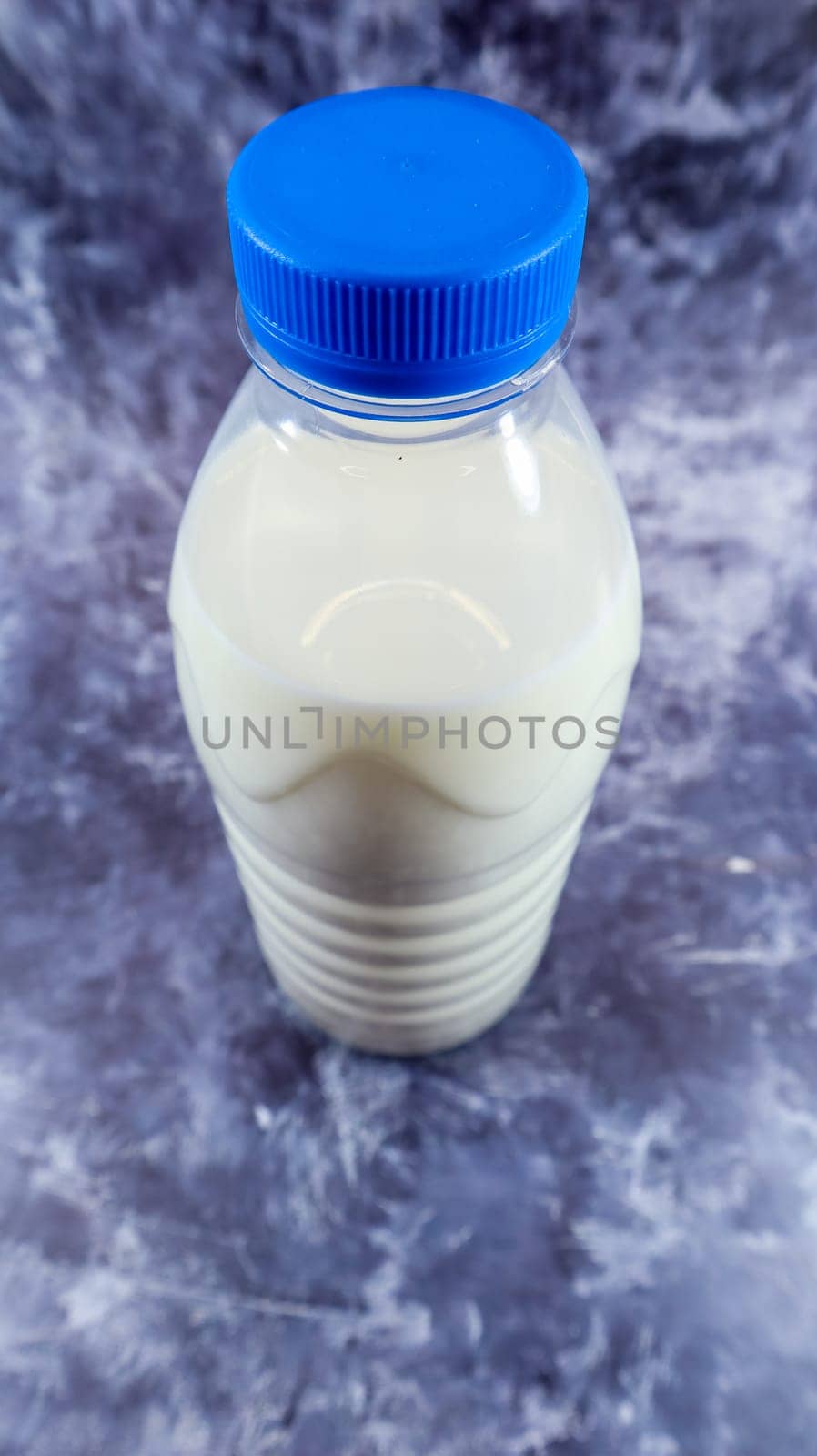 A plastic bottle of fresh regular milk on a dark gray marbled or concrete background. Close-up front view. World milk day concept. Nutrient fluid. Vertical photography