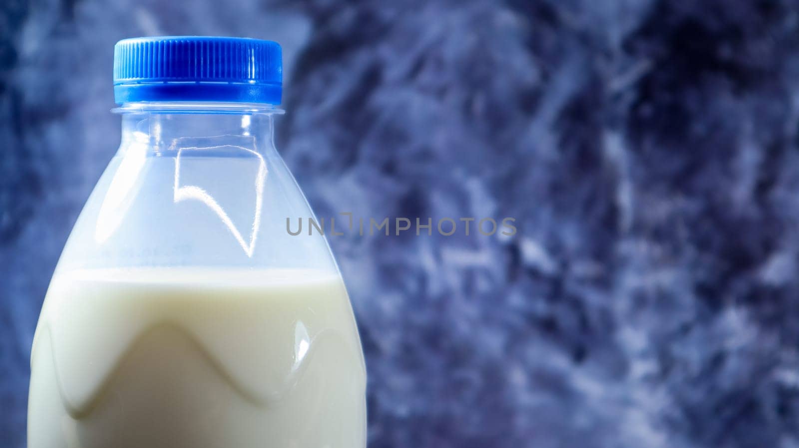 A plastic bottle of fresh regular milk on a dark gray marbled or concrete background. Close-up front view. World milk day concept. Nutrient fluid. Copy space