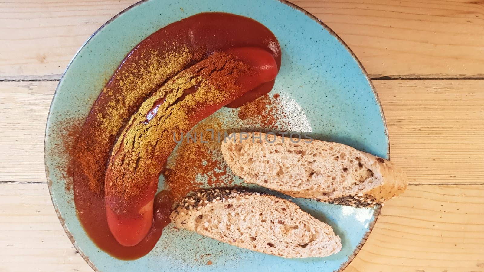 Traditional German currywurst in a plate on a wooden table in a cafe with bread. View from above. Specialties of Germany and Berlin. Sausage in spicy tomato red curry sauce.