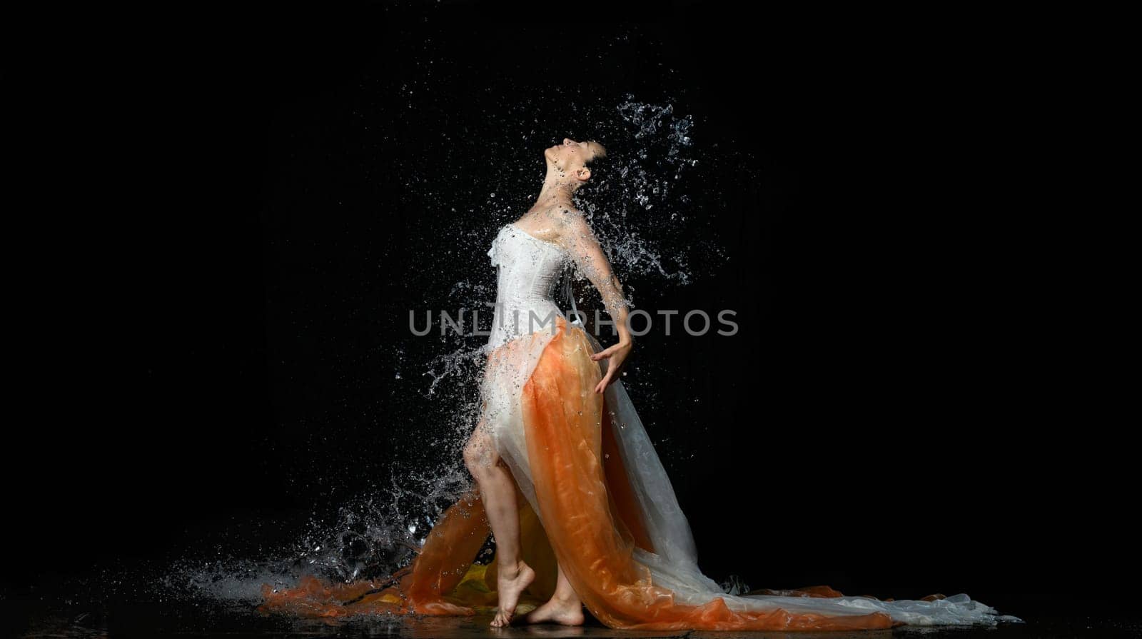 beautiful woman of Caucasian appearance with black hair dances in drops of water on a black background. Woman wearing white corset and skirt, passion pose