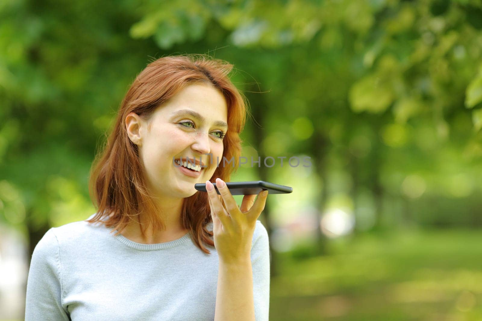 Happy woman uses voice recognition on smart phone walking in a park