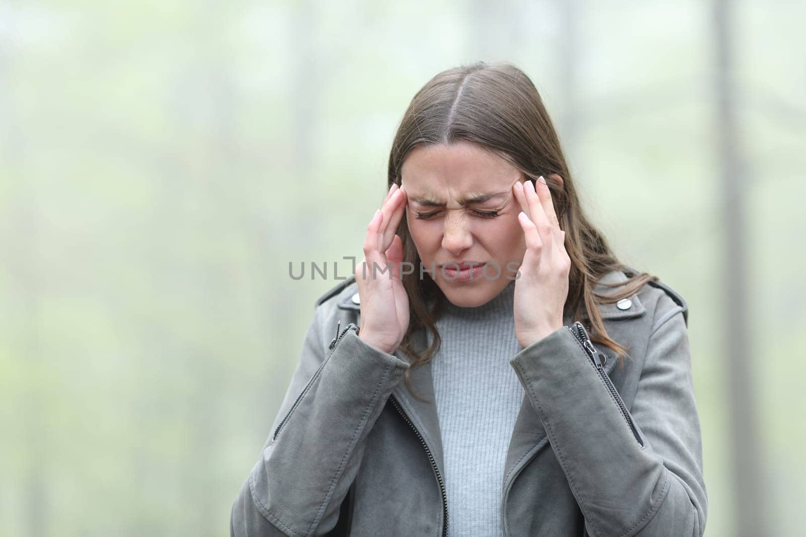 Stressed woman suffering migraine in a cold foggy day in a park