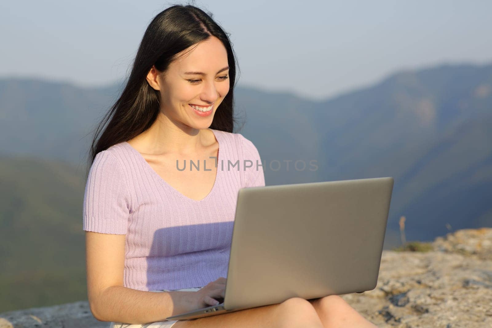 Happy asian woman using laptop sitting on a cliff in the mountain