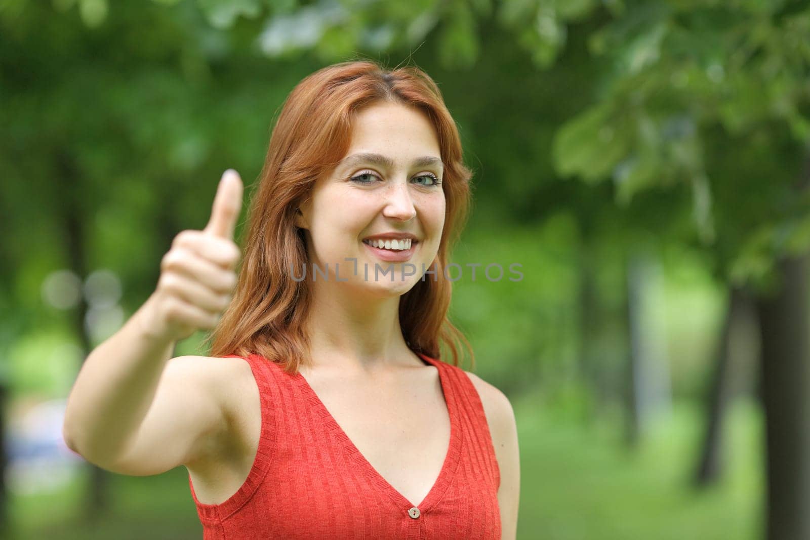 Happy woman gesturing thumbs up looking at camera in a park