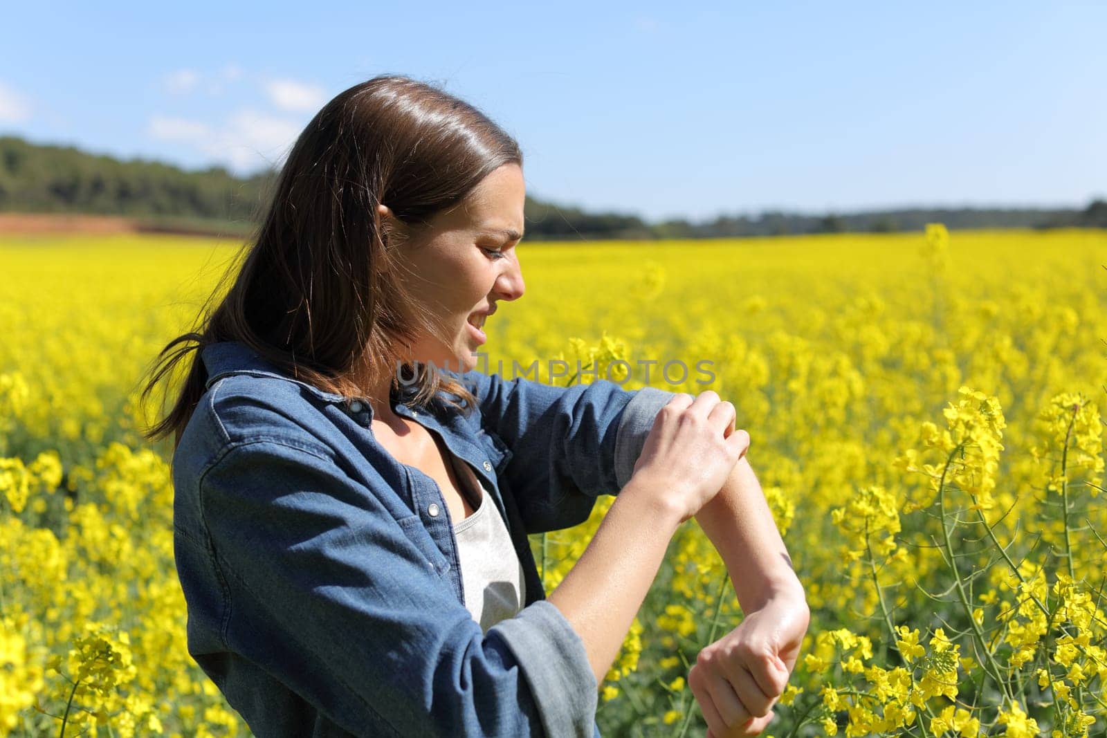 Stressed woman scratching arm in a field on summer
