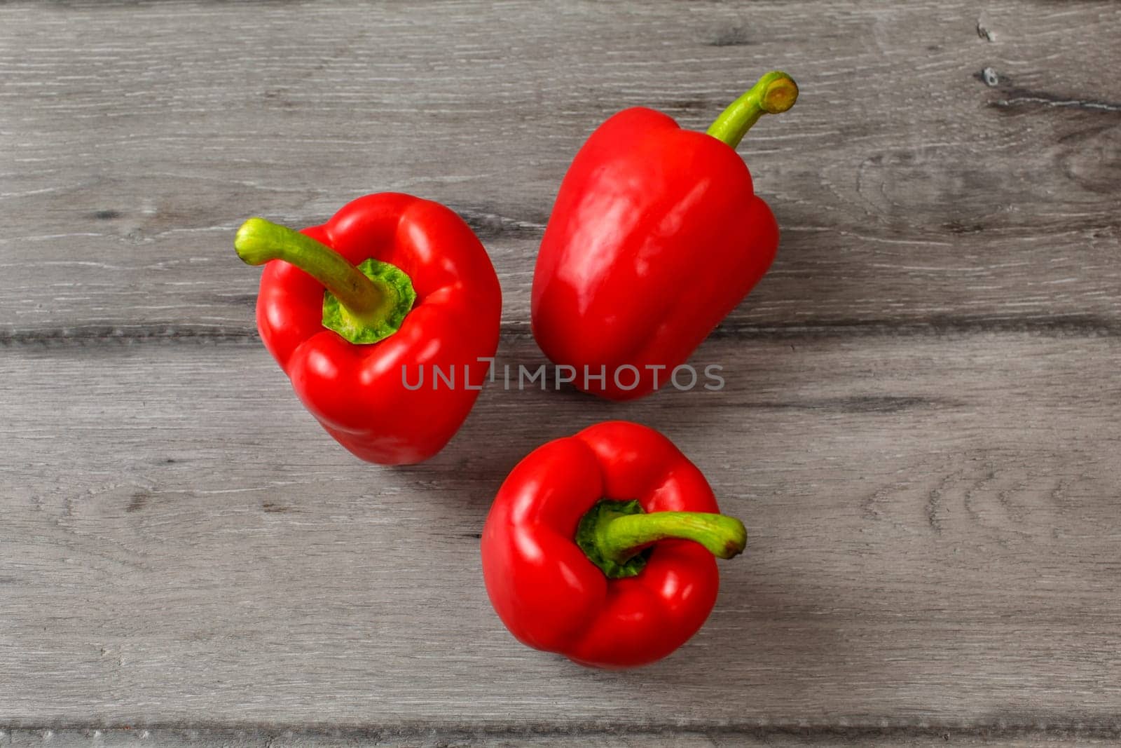 Table top view - three red bell peppers on gray wood desk.