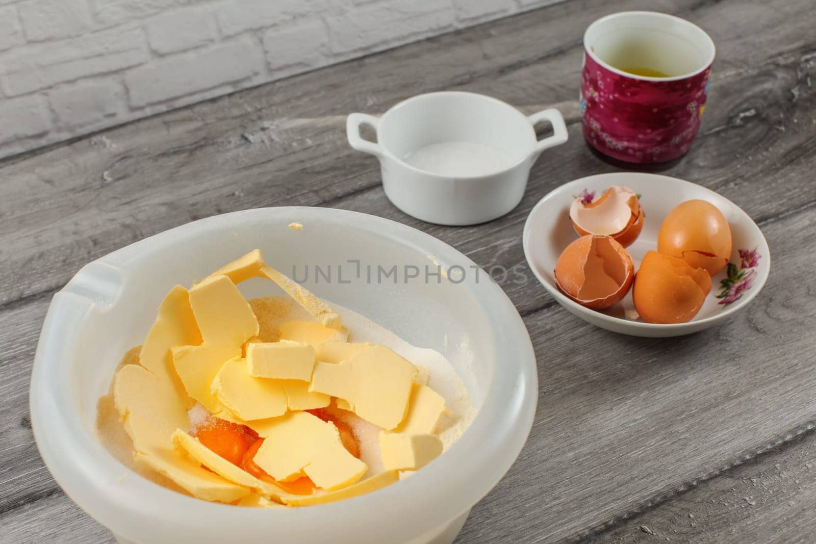 Cake preparation - plastic bowl with flour and yolk, egg shells and salt in background on gray wood table.