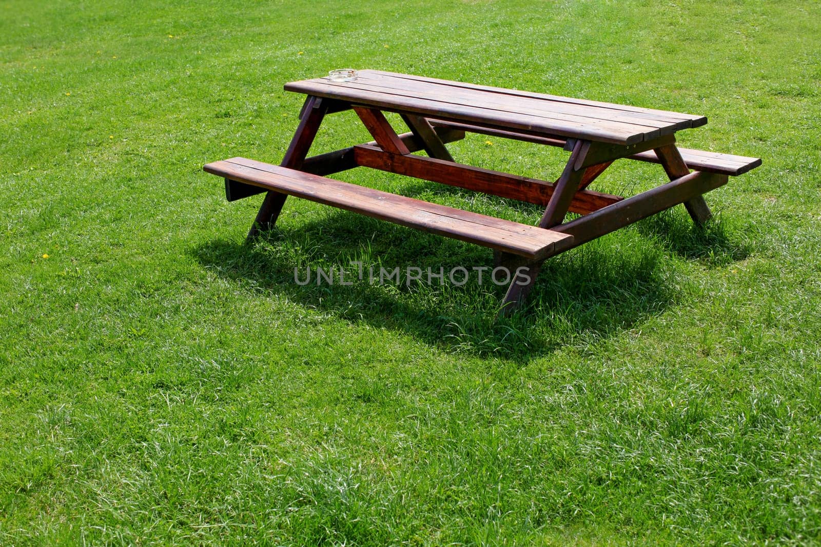 Garden furniture (picnic table - wooden desk and bench in one piece) with ashtray, on a green lawn.
