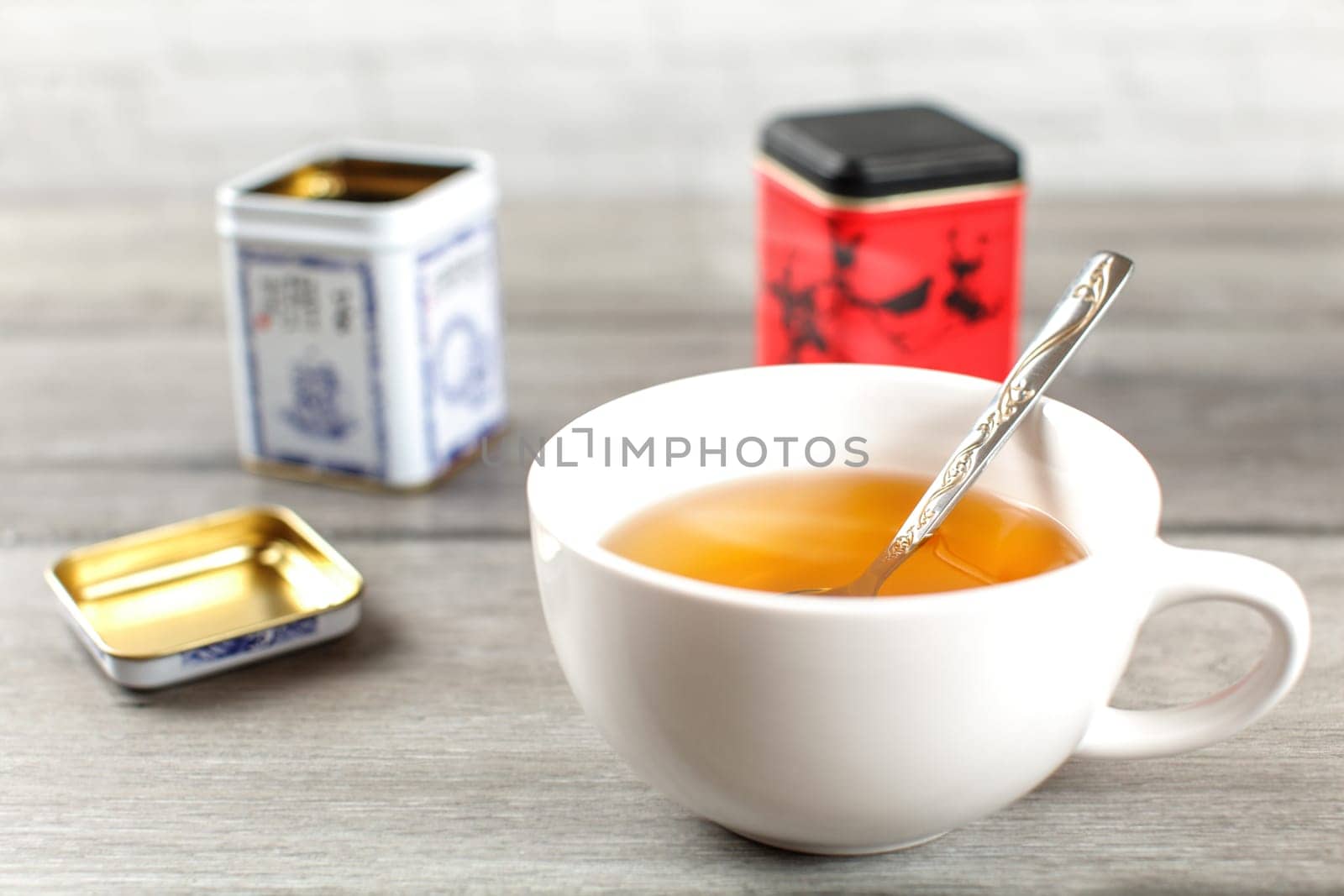 Cup of hot black tea, with metal loose leaf caddy in back, on gray wood desk.