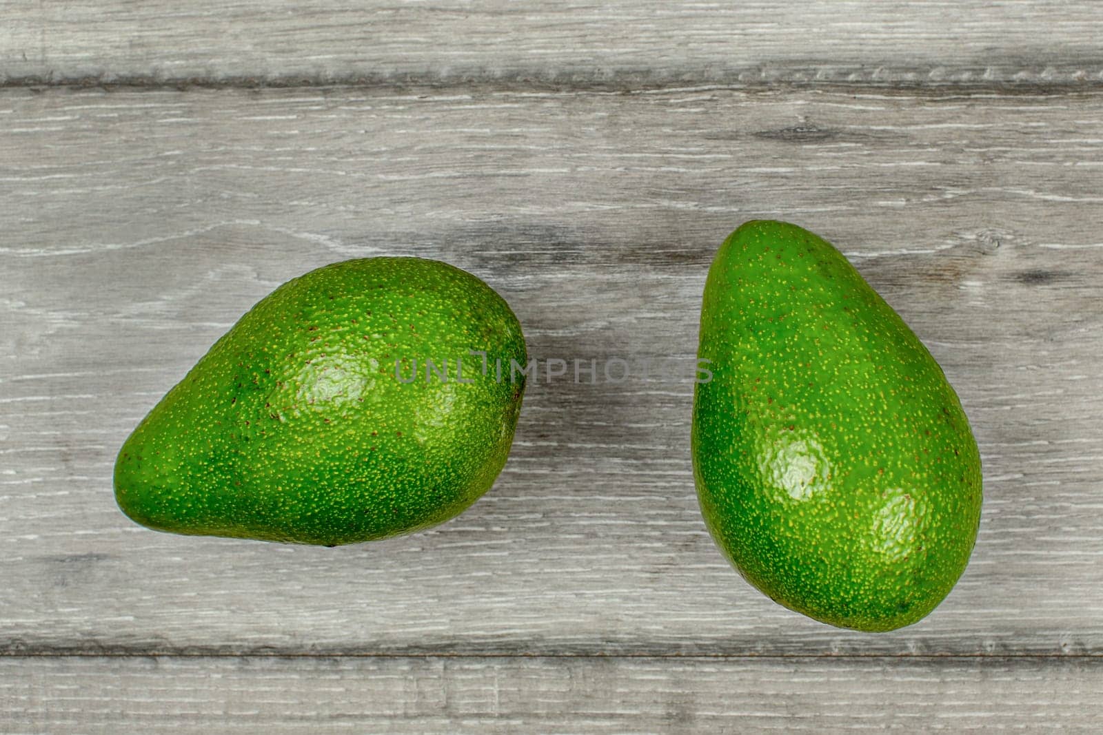 Table top view - two whole avocado fruits on gray wood desk.