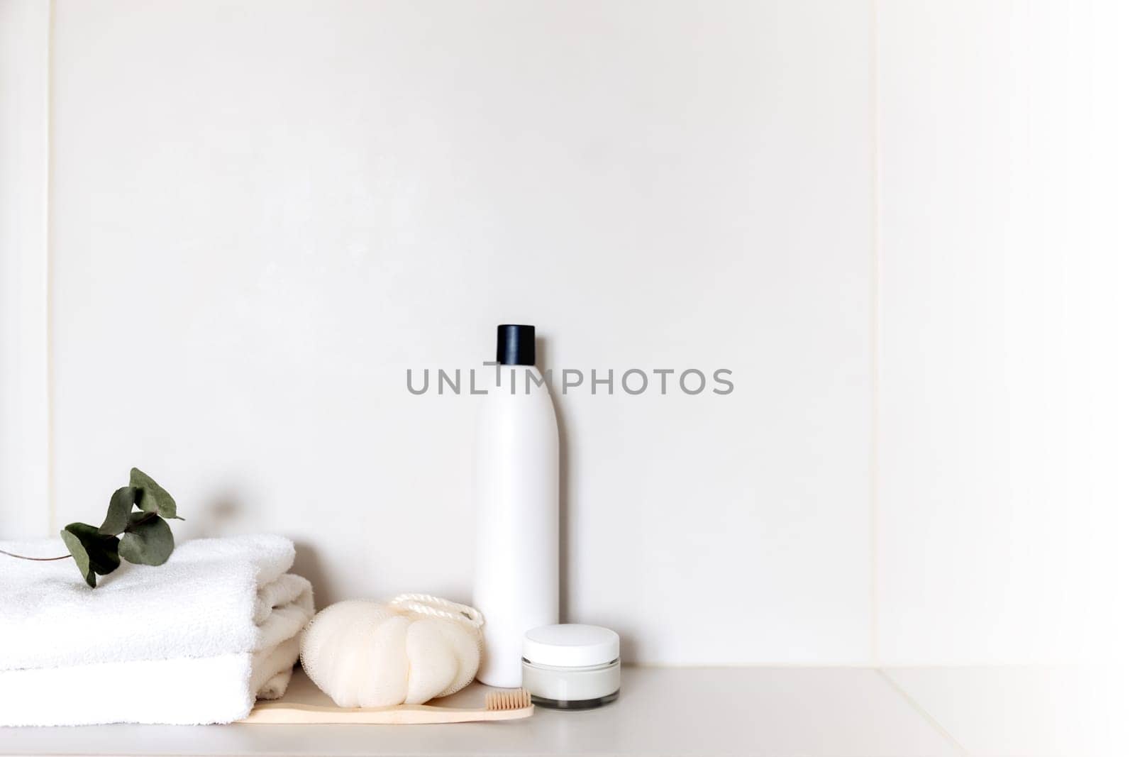 White bathroom shelf with different bath accessories. Hotel cleaning concept. Household concept. Washcloth, shampoo, cream, plant, toothbrush, brush, eucalyptus leaves on white towels. Body, skin care