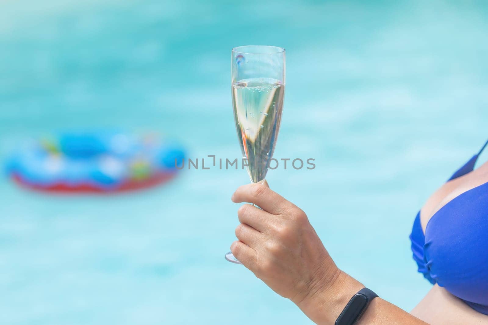 Female model is holding glass of champagne in the pool. Bathing ring is in the background.