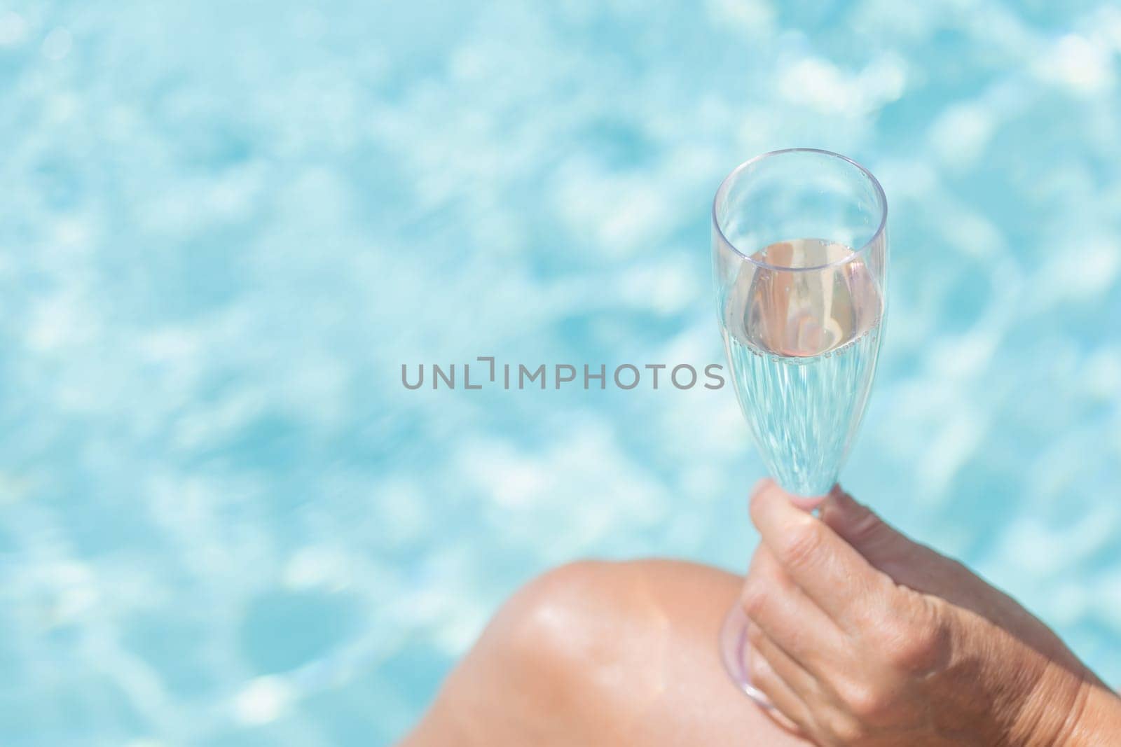 Hand of female model is holding glass of champagne. The pool level is in the background.