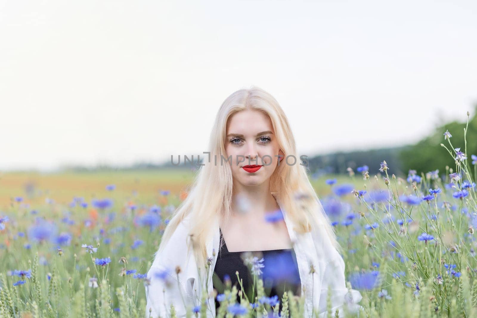 Front view portrait of attractive blonde woman in cornflower meadow. Horizontally.