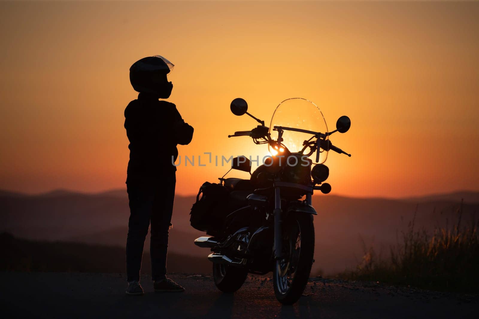 Motorcycle driver with her motorcycle in the sunset. Travel and sport, speed and freedom concept