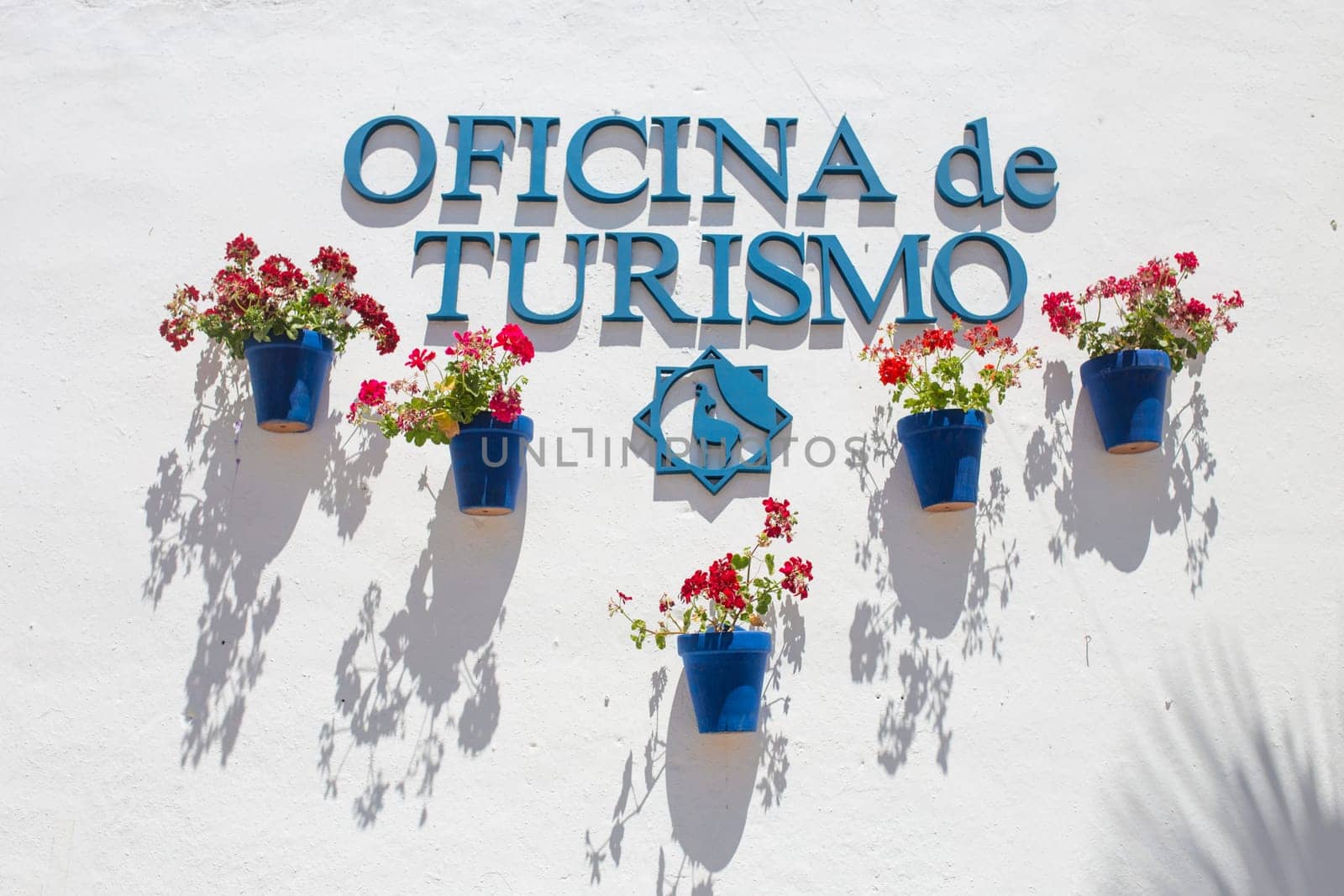 Cabra, Spain - May 19th, 2019: Cabra tourist office whitewashed wall full of attached blue flower pots, Cordoba, Spain. Typical andalusian architecture background