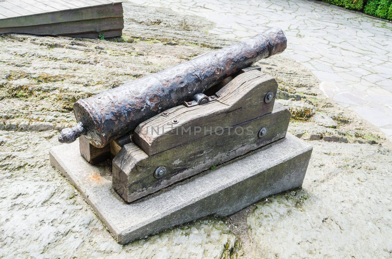 Antique cannon stands on the pier with paved paving stones against the background of the forest. Old cannon large. Ancient black cannon.