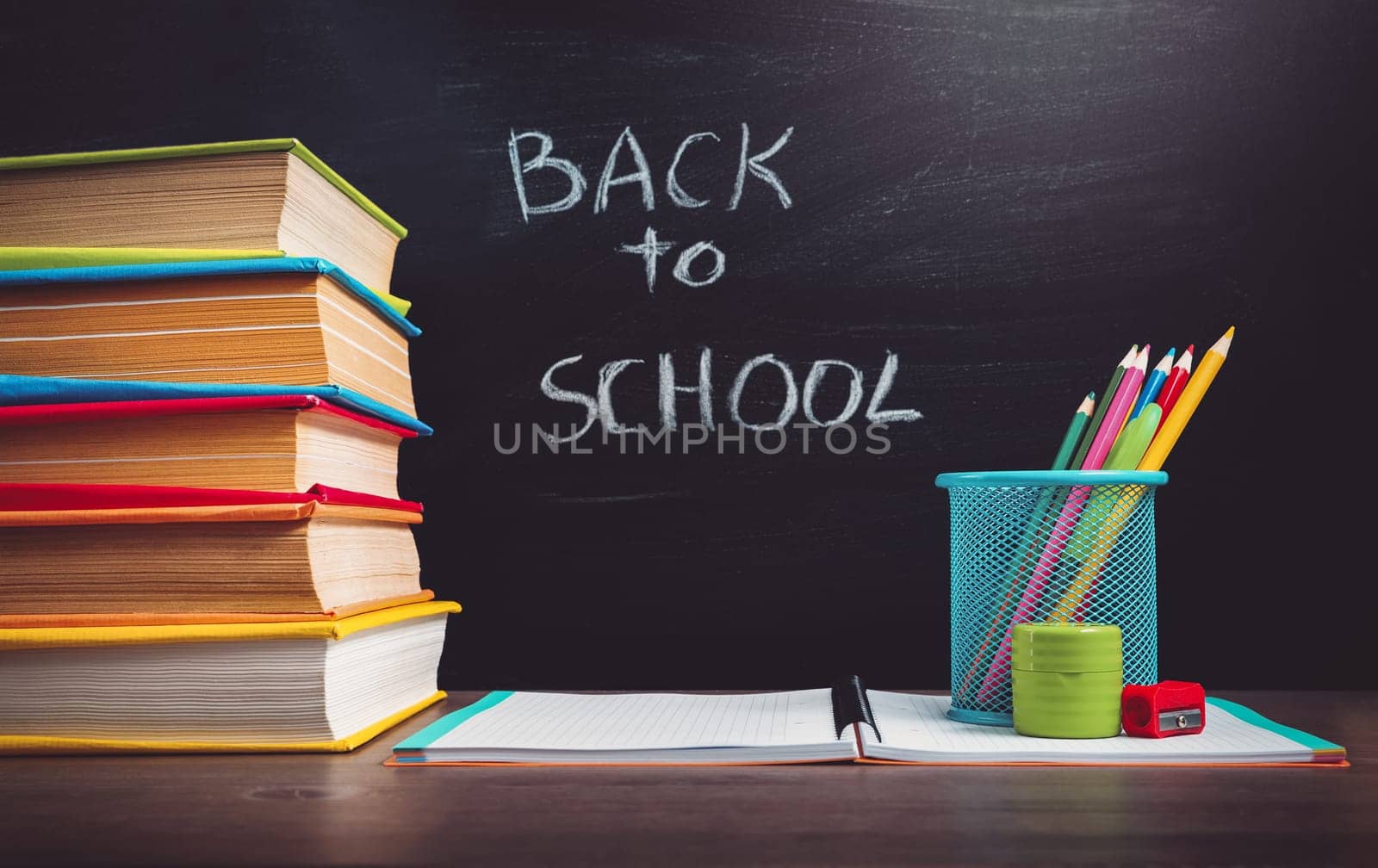 school accessories on the table with blackboard background. Pencils and books