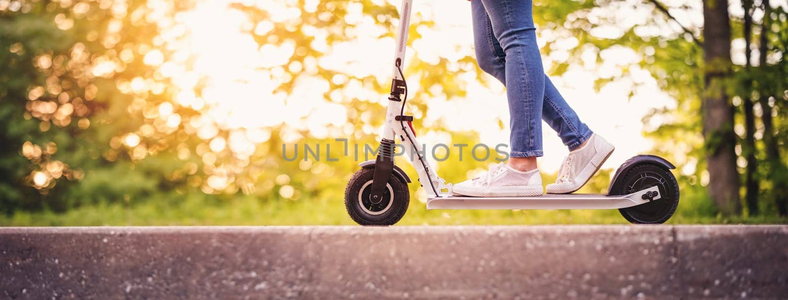Woman riding on scooter in park in summer. Urban eco transportation