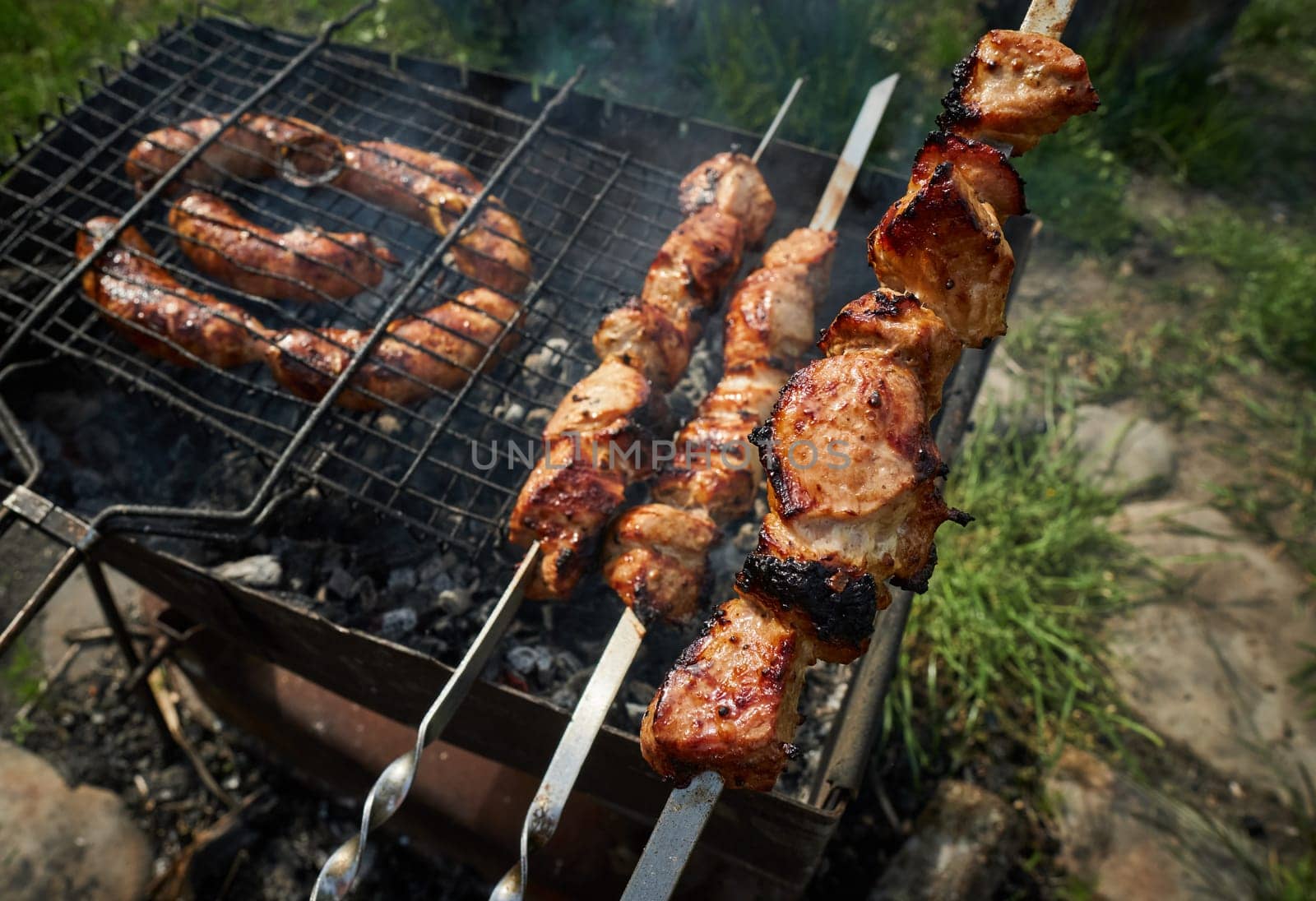 Man preparing shashlik or shish kebab over charcoal. Barbeque meat and sausages or bratwurst on a grill grate in backyard. Grilled meat on metal skewer outdoor. BBQ party or picnic food. Close up shot