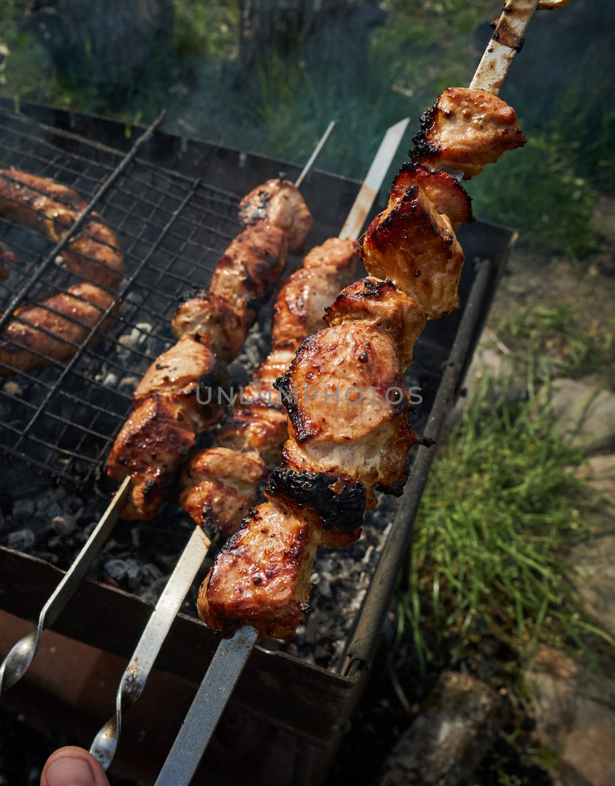 Man preparing shashlik or shish kebab over charcoal. Barbeque meat and sausages or bratwurst on a grill grate in backyard. Grilled meat on metal skewer outdoor. BBQ party or picnic food. Close up shot