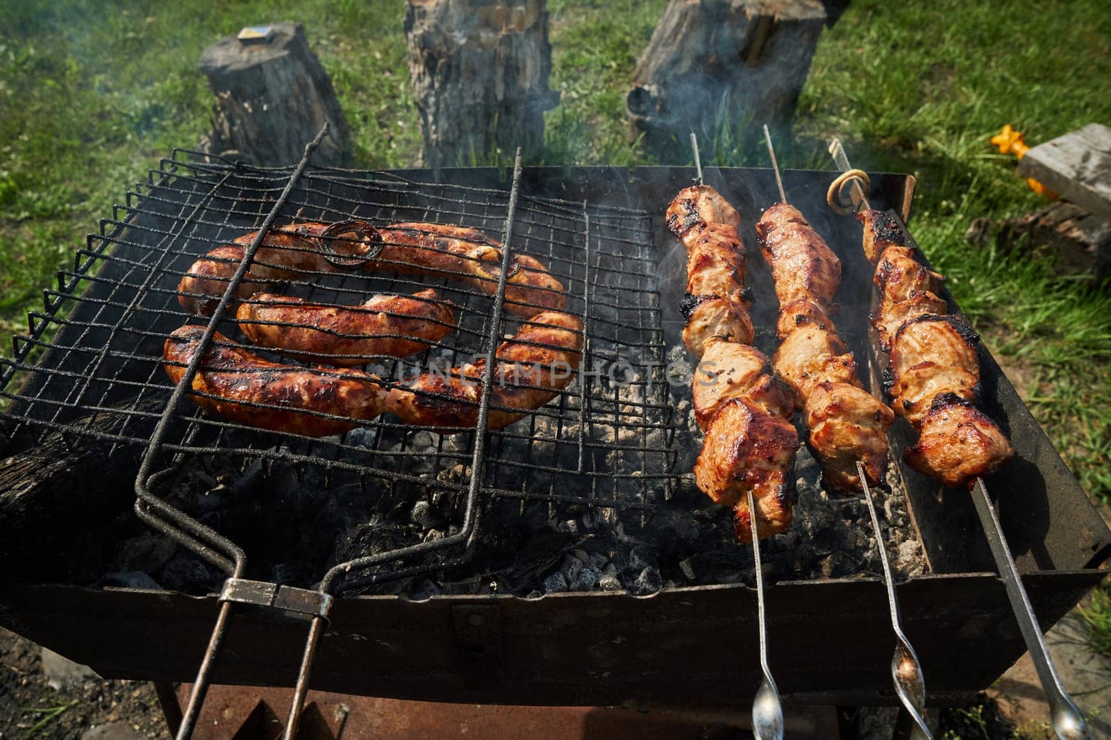 Man preparing shashlik or shish kebab over charcoal. Barbeque meat and sausages or bratwurst on a grill grate in backyard. Grilled meat on metal skewer outdoor. BBQ party or picnic food. Close up shot