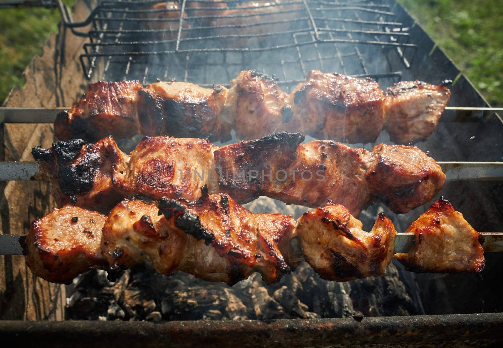 Man preparing shashlik or shish kebab over charcoal. Barbeque meat and sausages or bratwurst on a grill grate in backyard. Grilled meat on metal skewer outdoor. BBQ party or picnic food. Close up shot