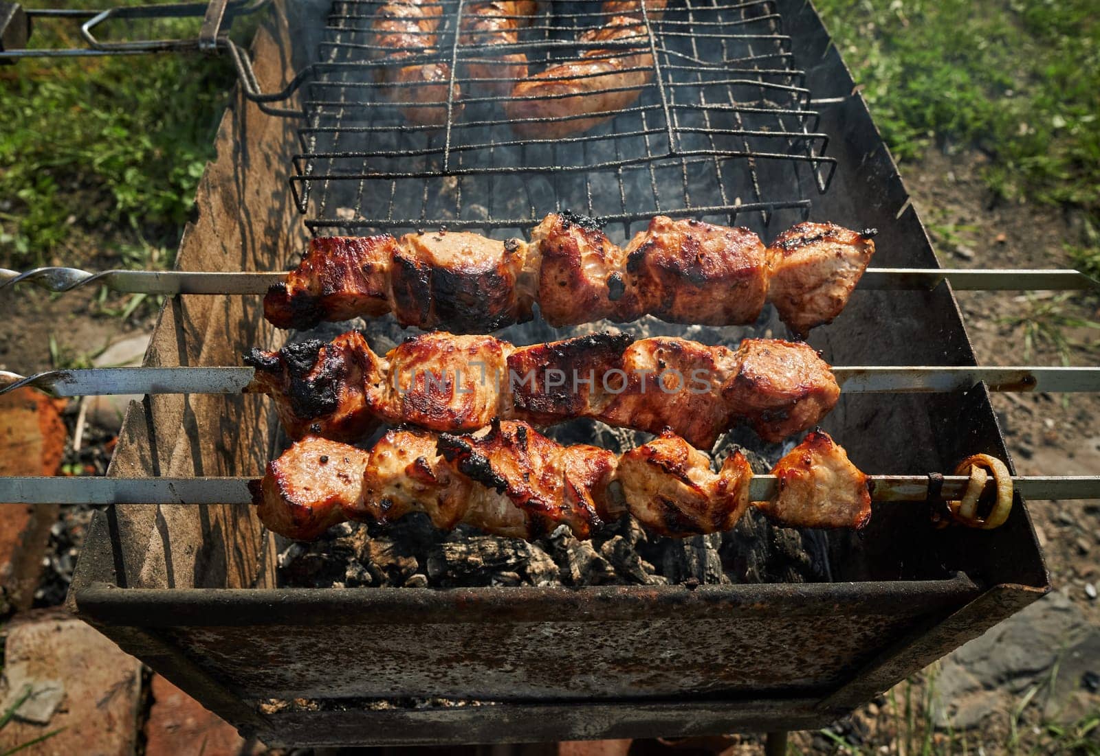 Man preparing shashlik or shish kebab over charcoal. Barbeque meat and sausages or bratwurst on a grill grate in backyard. Grilled meat on metal skewer outdoor. BBQ party or picnic food. Close up shot