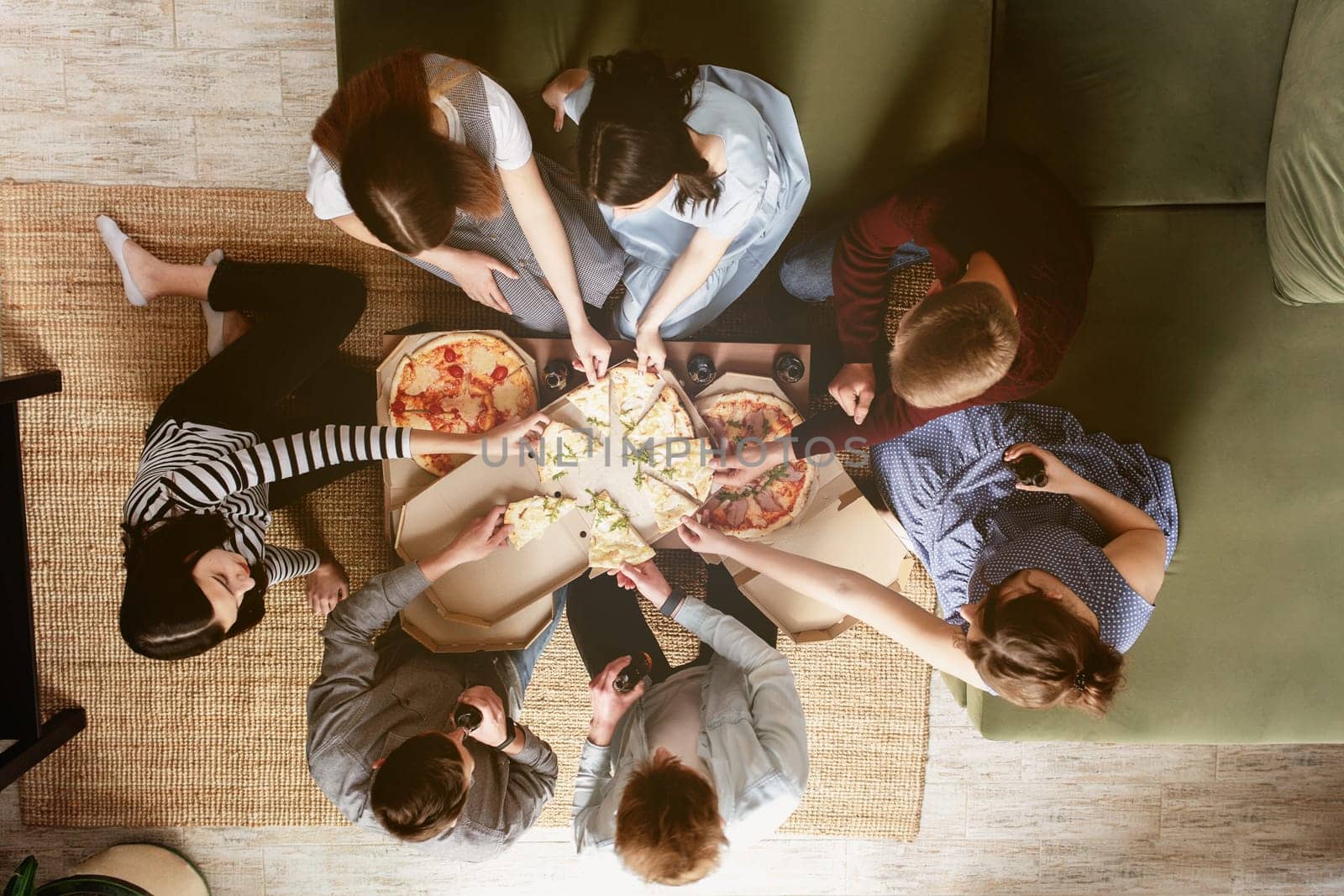 A pizza party, group of friends chatting and happily eating pizza at the table and drinking sweet soda water. Top view from the second floor. Many friends handing out together in green interior house