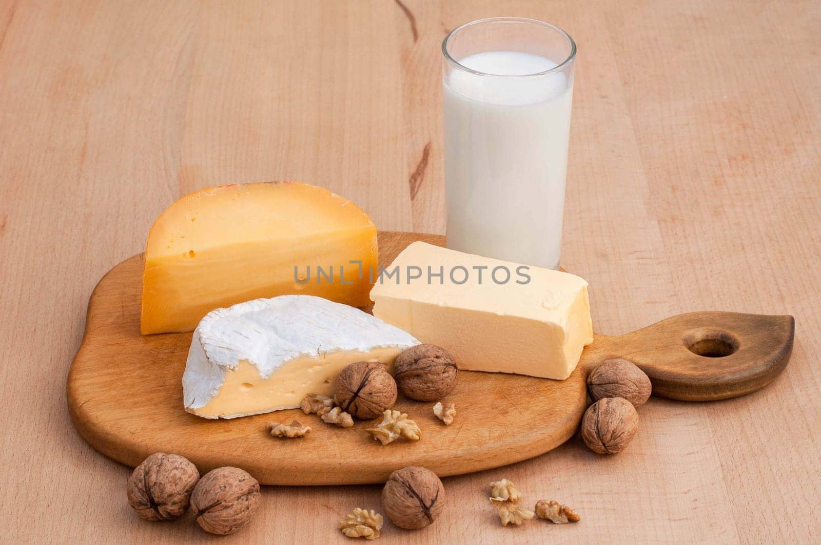 Camembert, Dutch cheese, walnuts, milk and butter on a wooden table