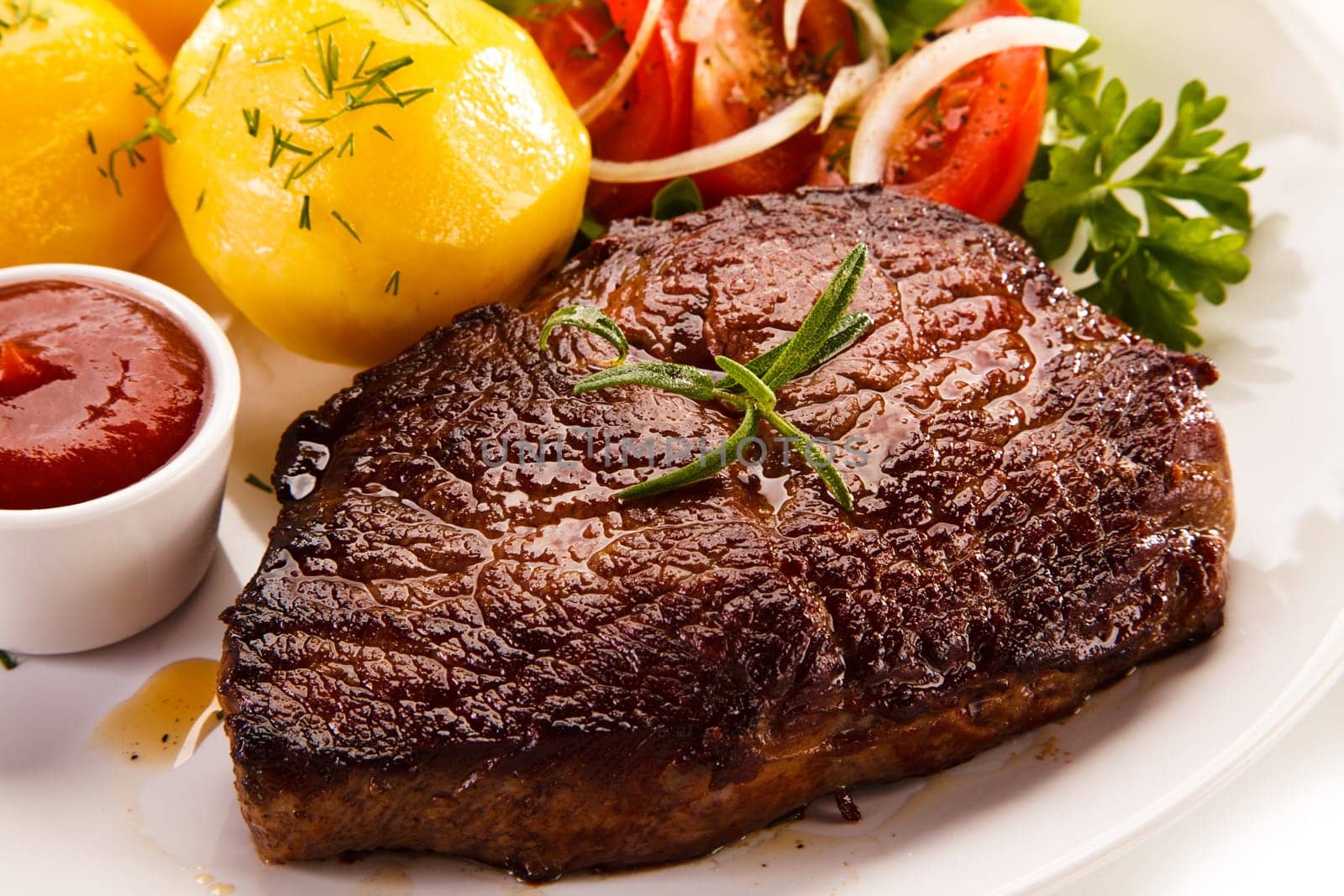 Grilled steaks, boiled potatoes and vegetable salad on white bac
