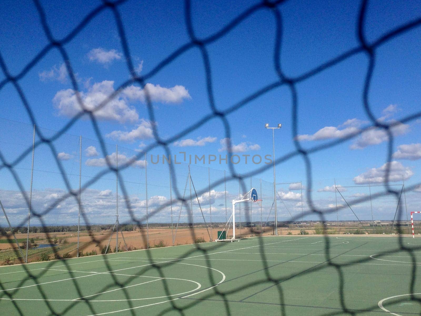 Urban multisports court seen behind safety net. Blue cloudy sky