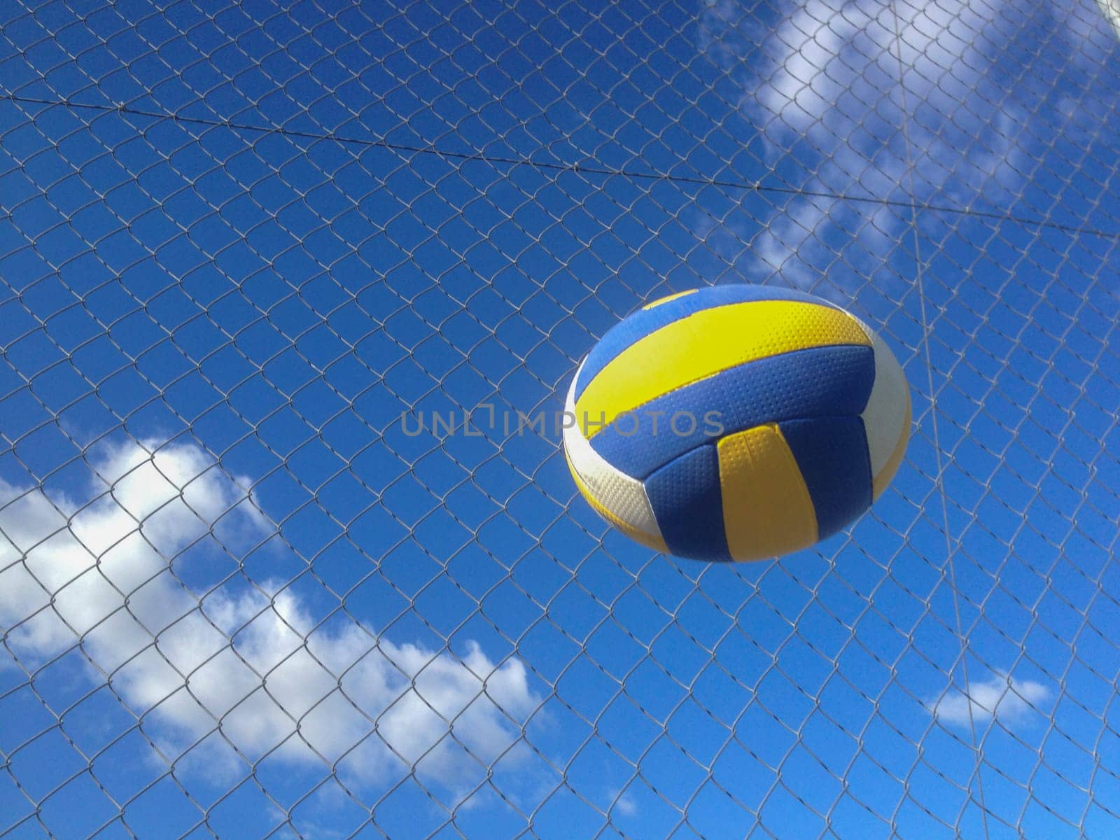 Volleyball ball in the air over wire fence background. Motion deformated object