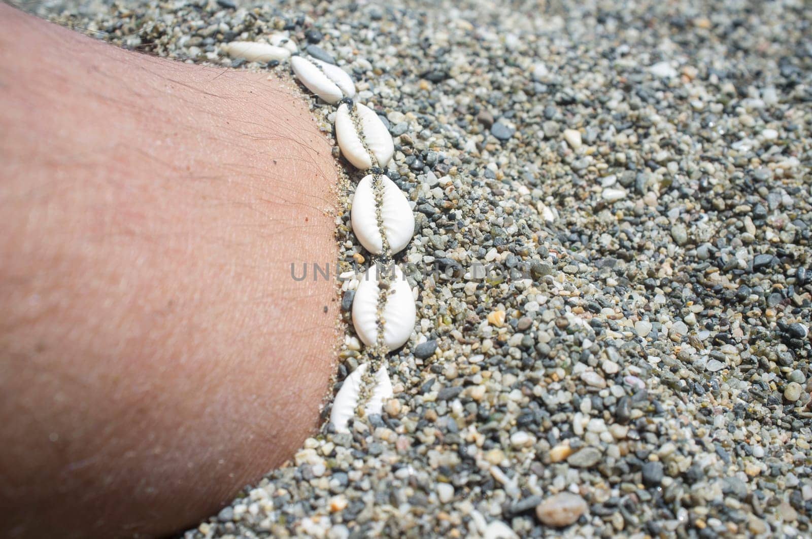 Shell ankle bracelet on half buried male leg. Symbol of summertime