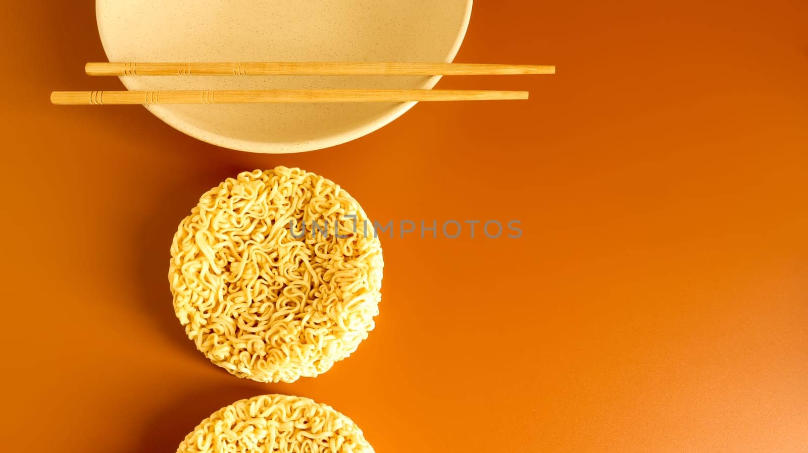 dry instant noodles in a typical circle shape on a plate with chopsticks. The effect of instant noodles on human health. pasta, for the preparation of which it is enough to pour boiling water.
