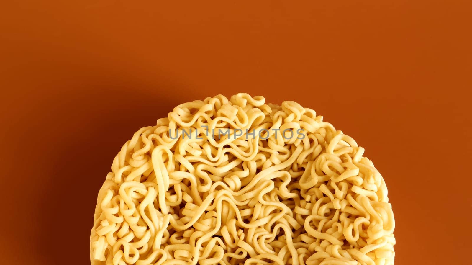 Korean instant noodles in the shape of a circle on a brown background. A yellowish-white dried raw vermicelli with long round lines and twisted in different directions into a briquette