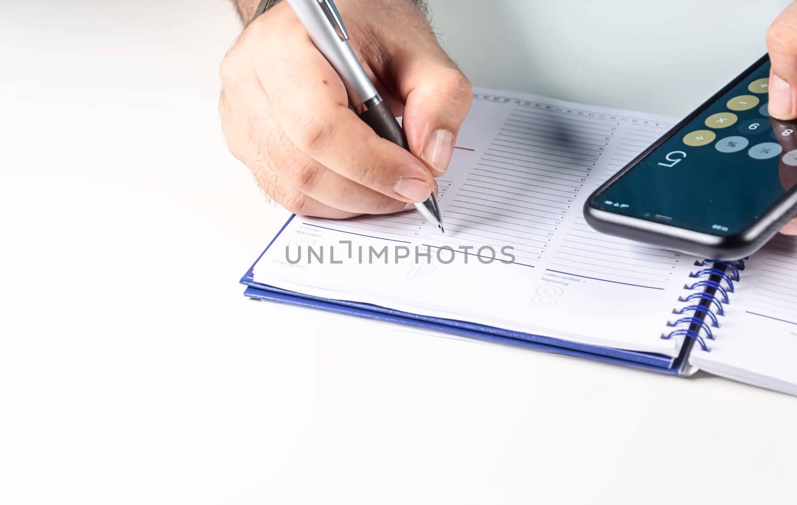 Man doing calculations with his mobile phone calculator and writing in a ring binder notebook with a pen. Budget and economy.