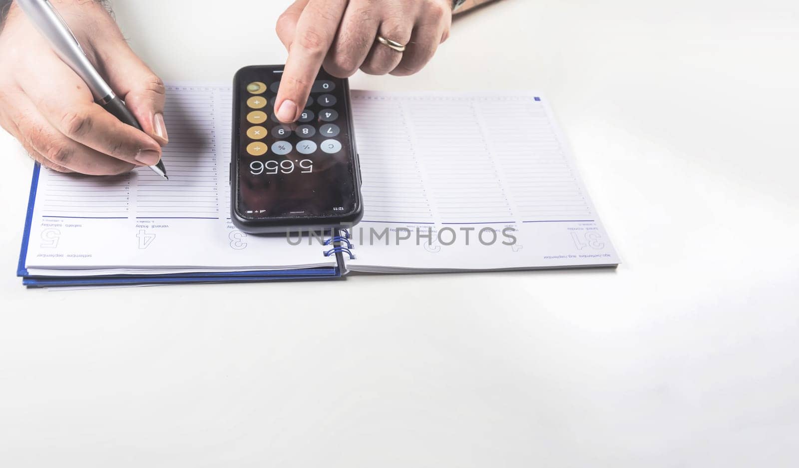 Man doing calculations with his mobile phone calculator and writing in a ring binder notebook with a pen. Budget and economy.