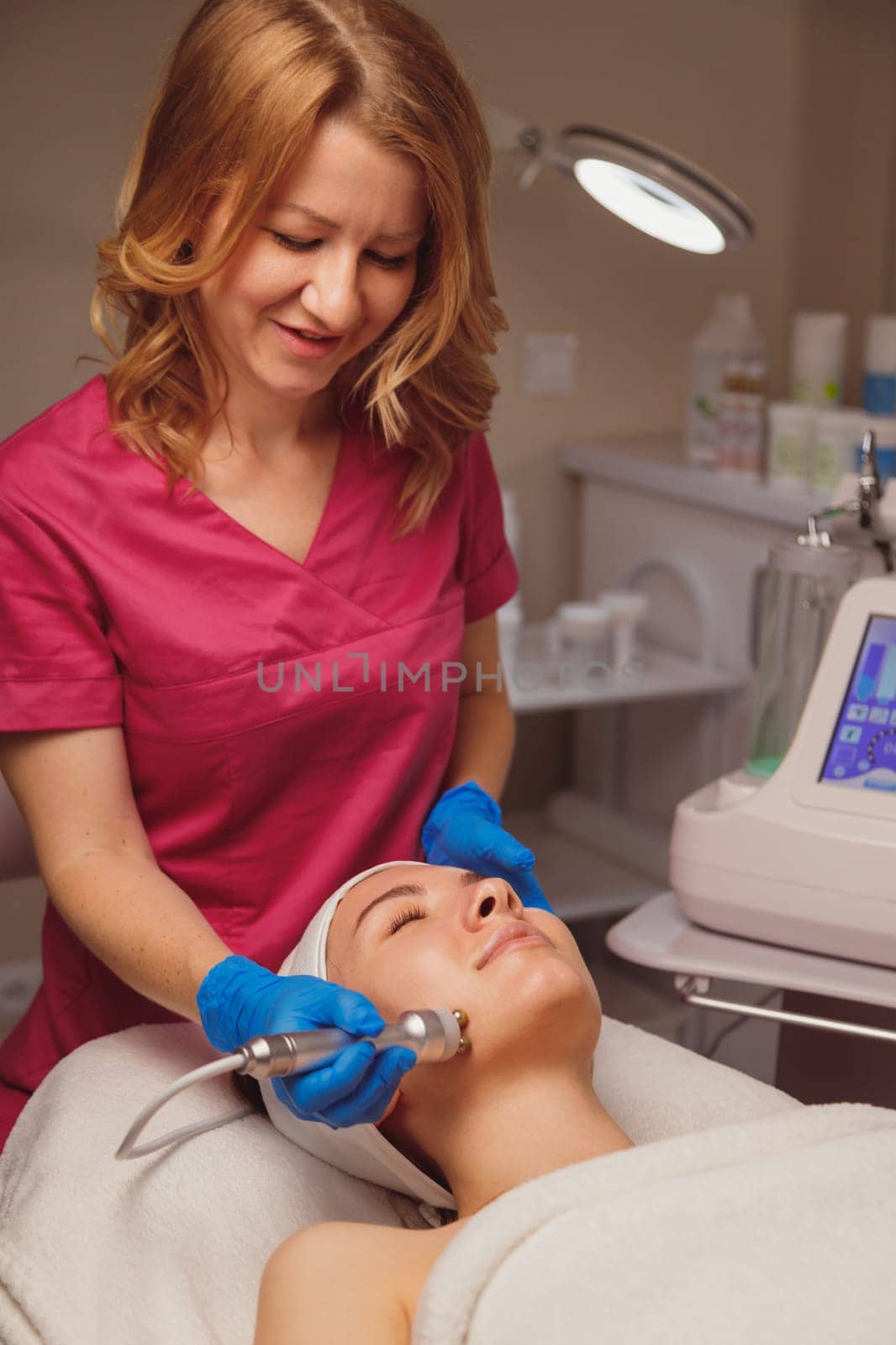 Young woman getting microcurrents skin cleansing and face treatment at beauty salon.