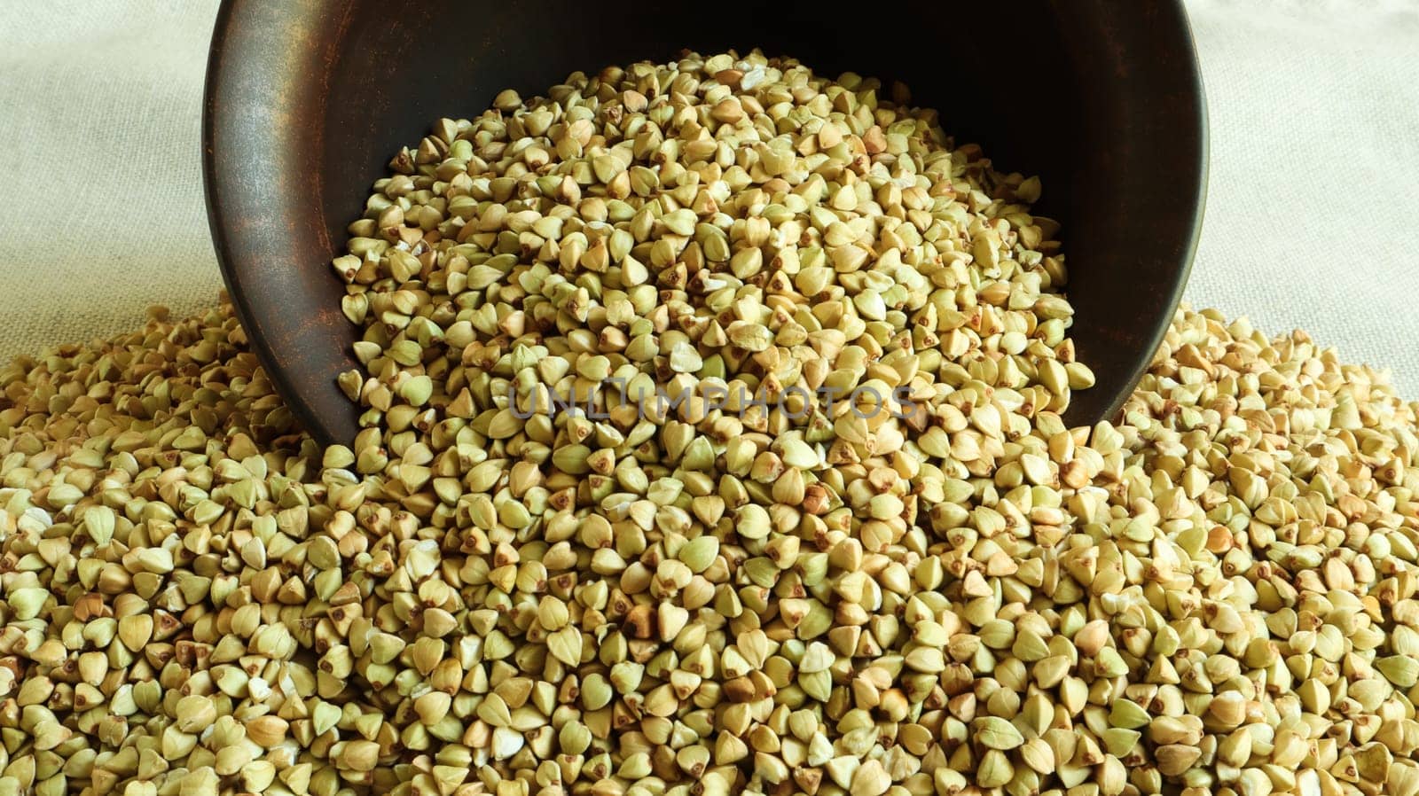 Buckwheat scattered background, raw green buckwheat in a brown clay bowl or plate. Healthy groats. Organic raw non-fried vegetarian food. The concept of a healthy and balanced diet. Diet food.