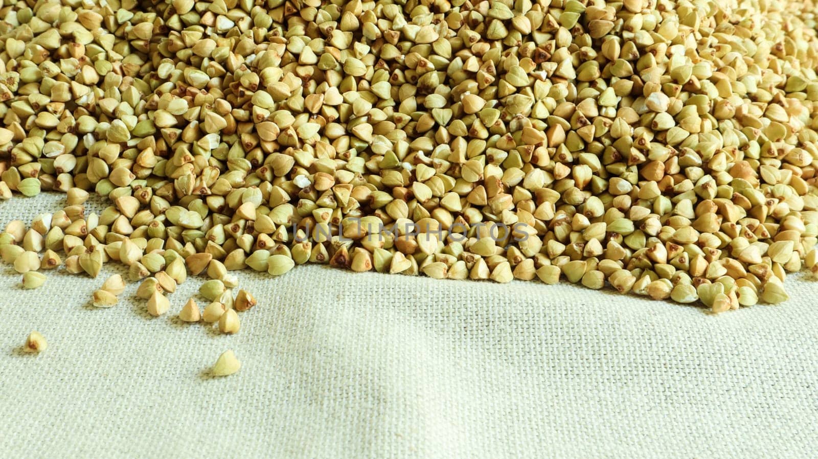 Background from raw organic green buckwheat porridge, vegan food. Texture of scattered buckwheat groats. Seeds are triangular in shape. Organic food. The concept of diet, weight loss, healthy eating