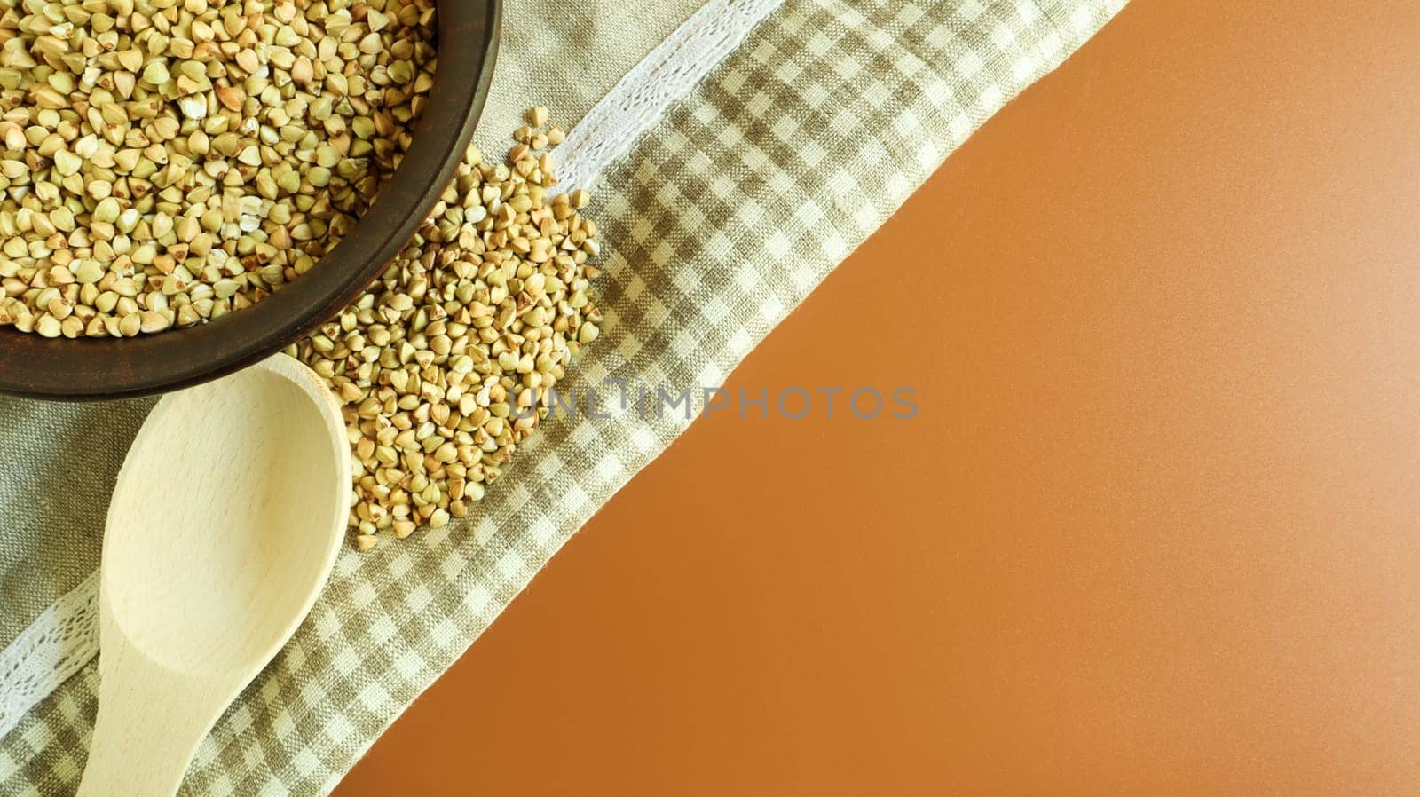 Raw green buckwheat in a brown clay plate and a wooden spoon. Vegan organic food concept. The concept of diet, weight loss, healthy and proper nutrition. Copy space for text. Top view, flat lay.