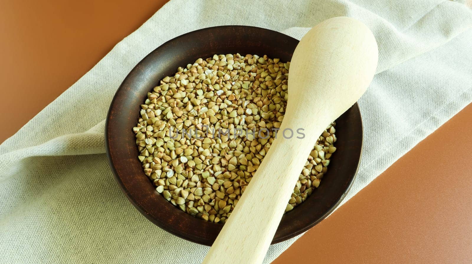 Raw green buckwheat in a brown clay plate and a wooden spoon. Vegan organic food concept. The concept of diet, weight loss, healthy and proper nutrition. Copy space for text. Top view, flat lay.