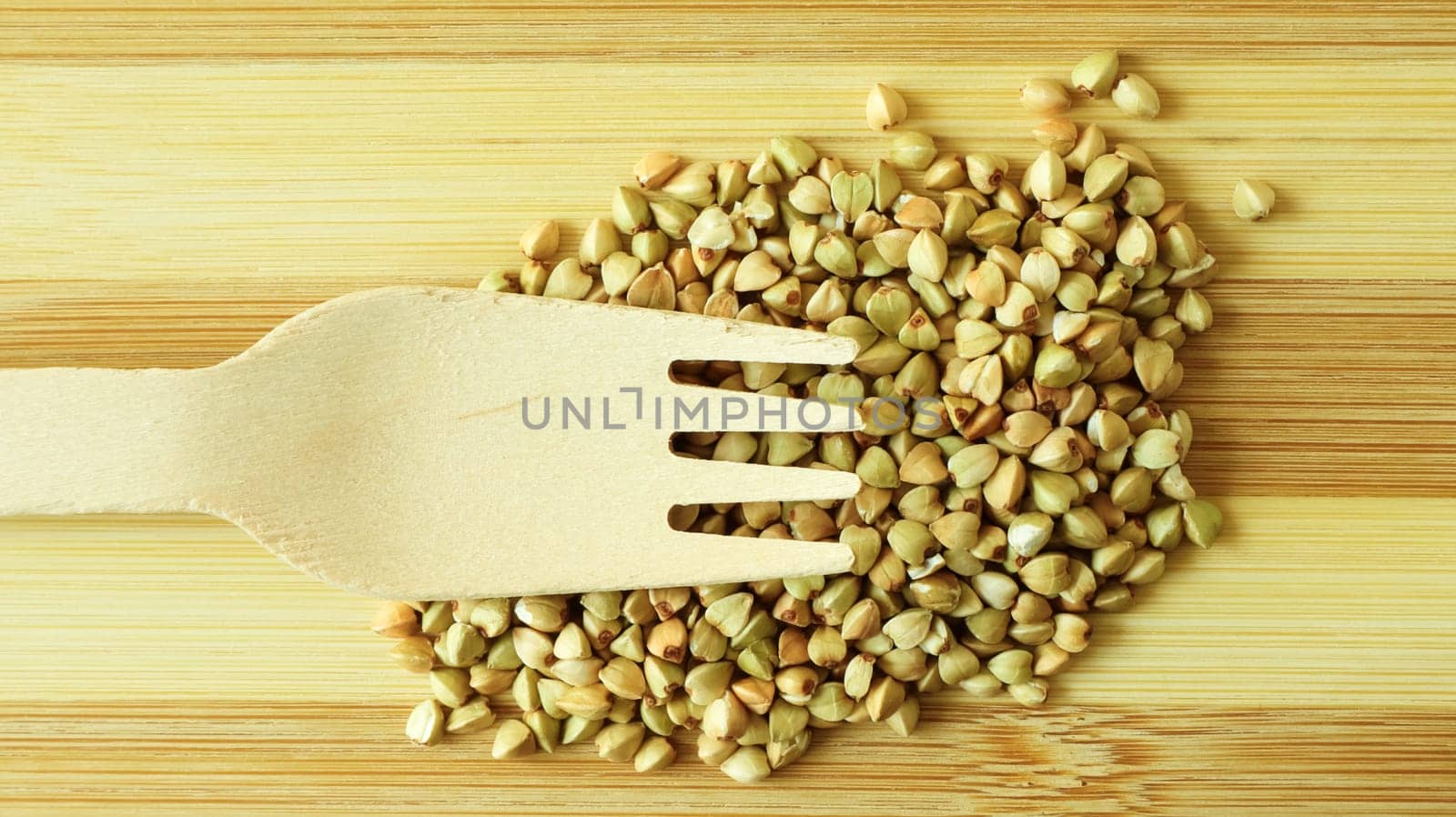 Raw green organic buckwheat on a wooden background with a wooden fork. Dietary nutrition. Copy space Concept of vegetarianism, balanced and healthy diet