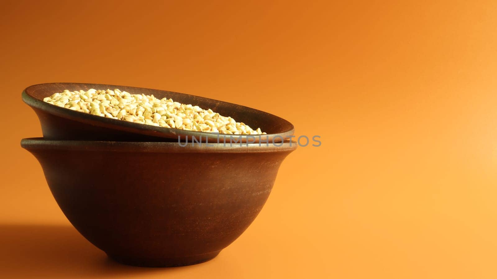 Raw green buckwheat in a brown clay plate on a brown background. Vegan organic food concept. The concept of diet, weight loss, healthy and proper nutrition. Copy space for text or logo