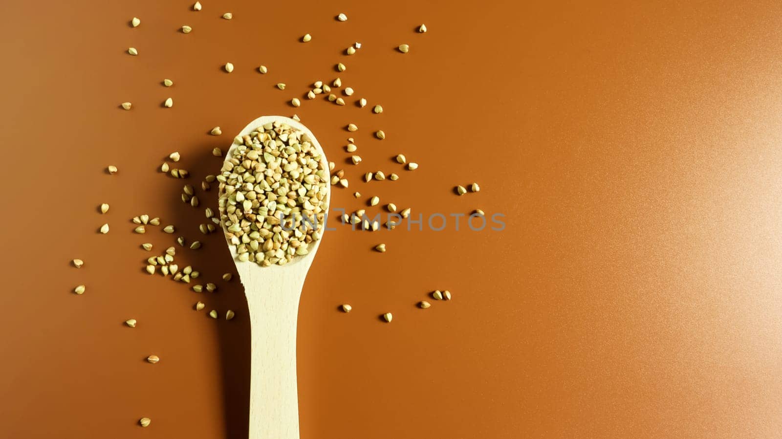 Green buckwheat in a wooden spoon on a brown background. Great food. healthy groats. Organic raw non-fried vegetarian food. The concept of a healthy and balanced diet. Dietary foods. Copy space.