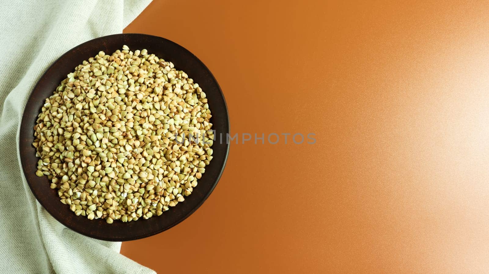 Raw green buckwheat in a brown clay plate on a brown background. Vegan organic food concept. The concept of diet, weight loss, healthy and proper nutrition. Copy space for text. Top view, flat lay.
