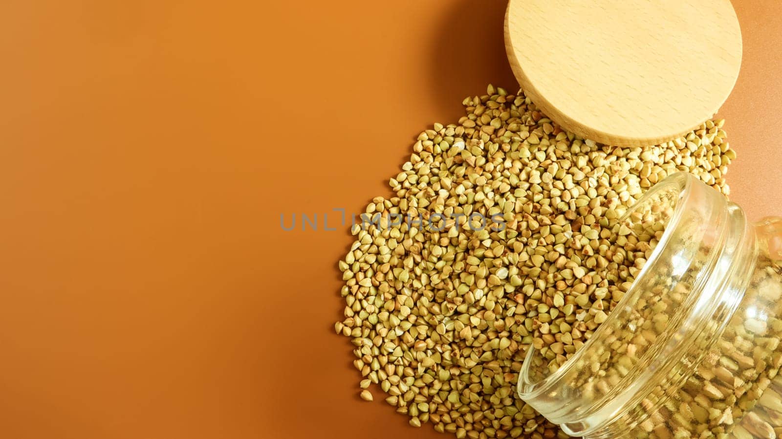 Scattered raw green buckwheat with a glass jar for cereals. Vegan organic food concept. The concept of diet, weight loss, healthy and proper nutrition. Triangle shaped scatter kernels.