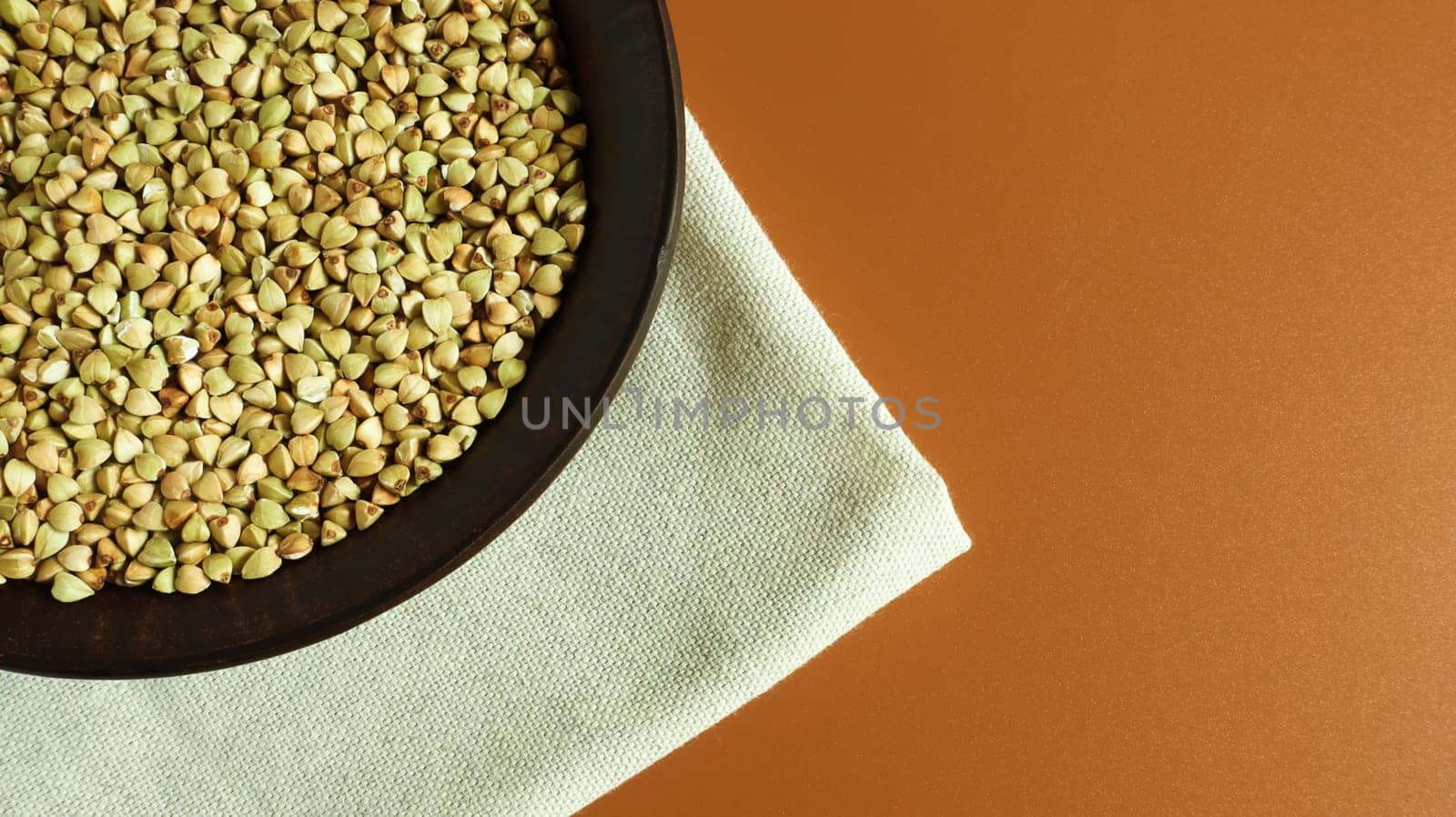Raw green buckwheat in a brown clay plate on a brown background. Vegan organic food concept. The concept of diet, weight loss, healthy and proper nutrition. Copy space for text. Top view, flat lay.